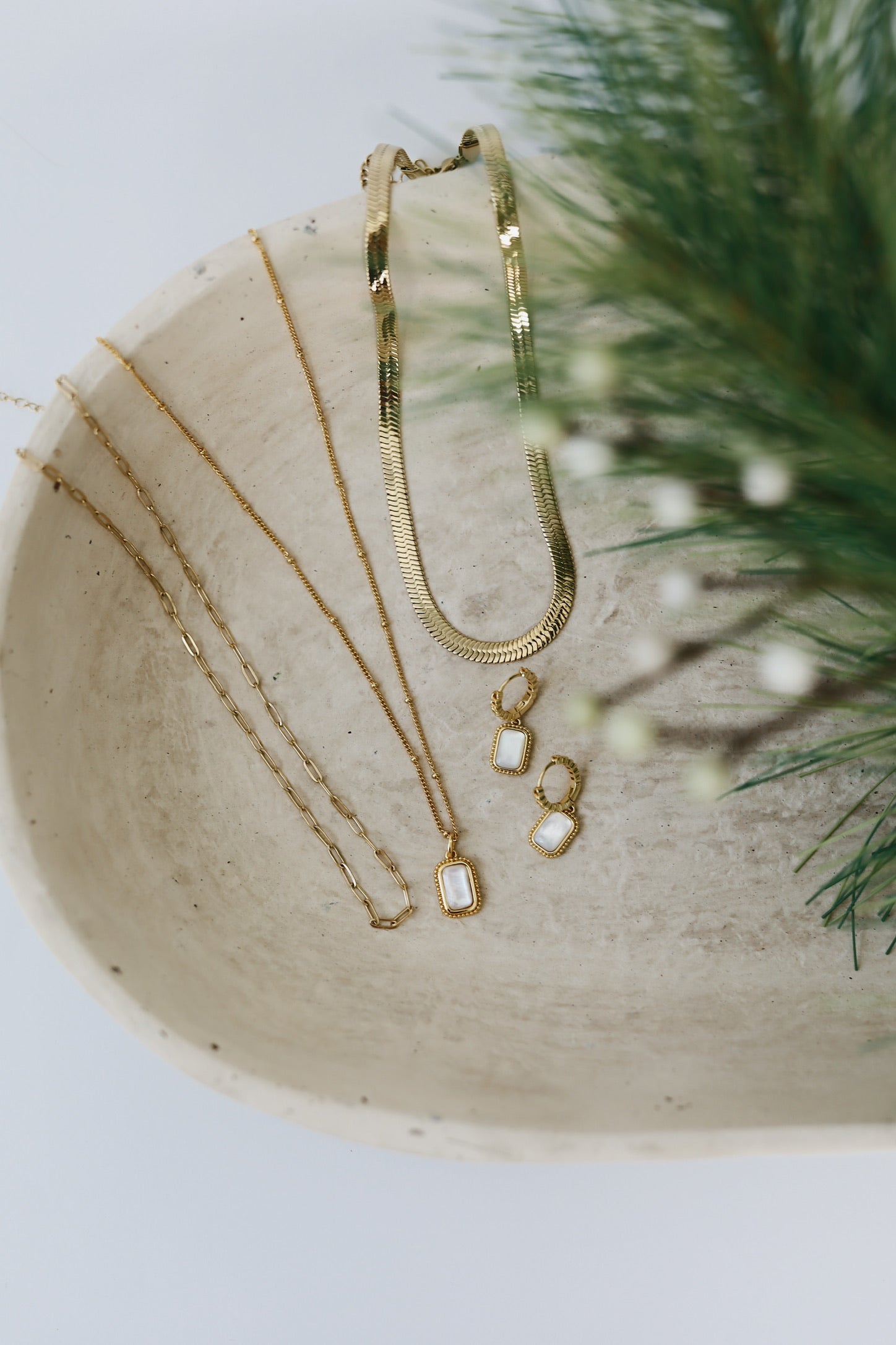 gold filled pearl jewelry on a tan tray with a pine tree branch