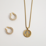 Gold necklace with a pendant and pearl hoop earrings on a light gray background