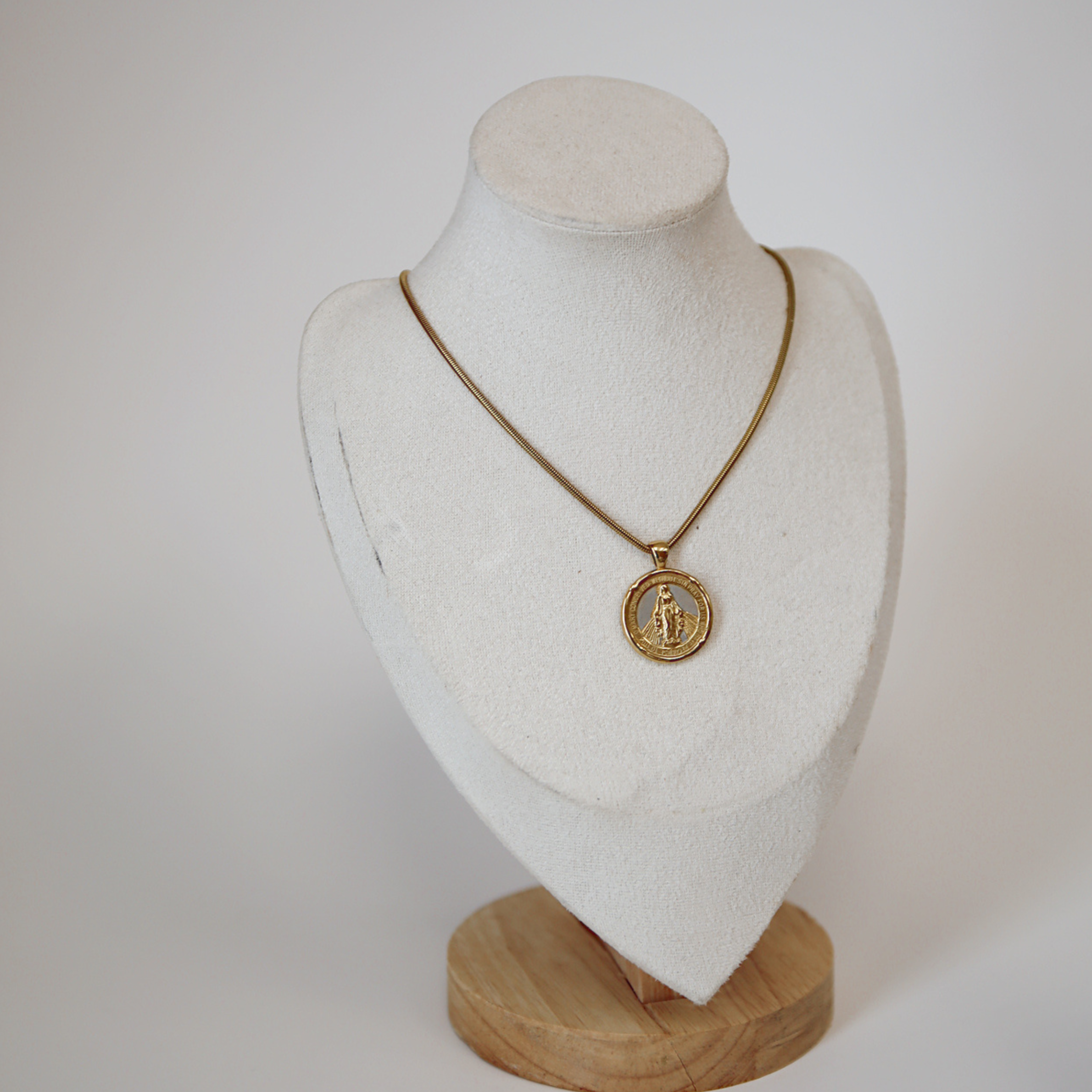 Gold necklace with a pendant on a white mannequin bust against a white background