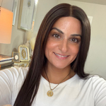 Woman with long brown hair wearing a gold necklace indoors.
