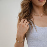 woman wearing a grey tanktop with 2 gold bracelets and 2 layered necklaces.